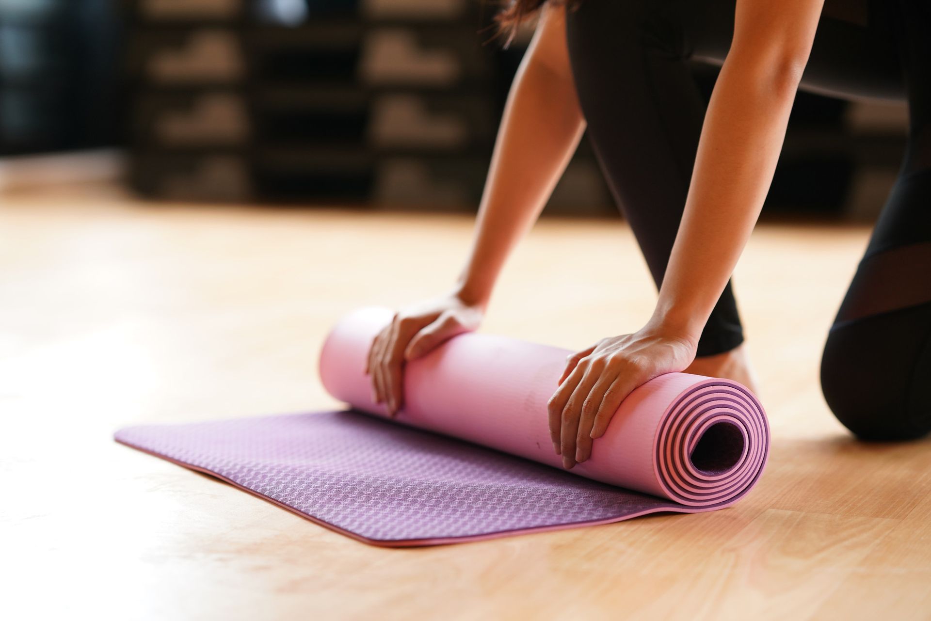 a woman is rolling a pink yoga mat on the floor .