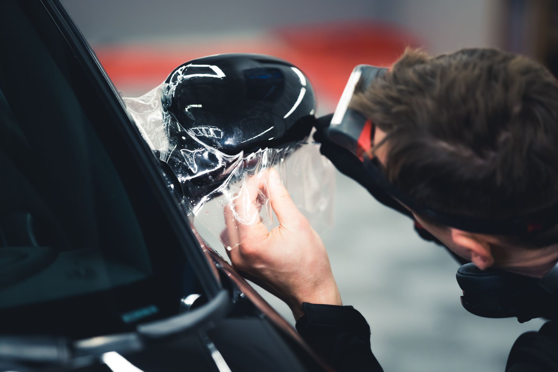 A man is applying a protective film to the side mirror of a car.