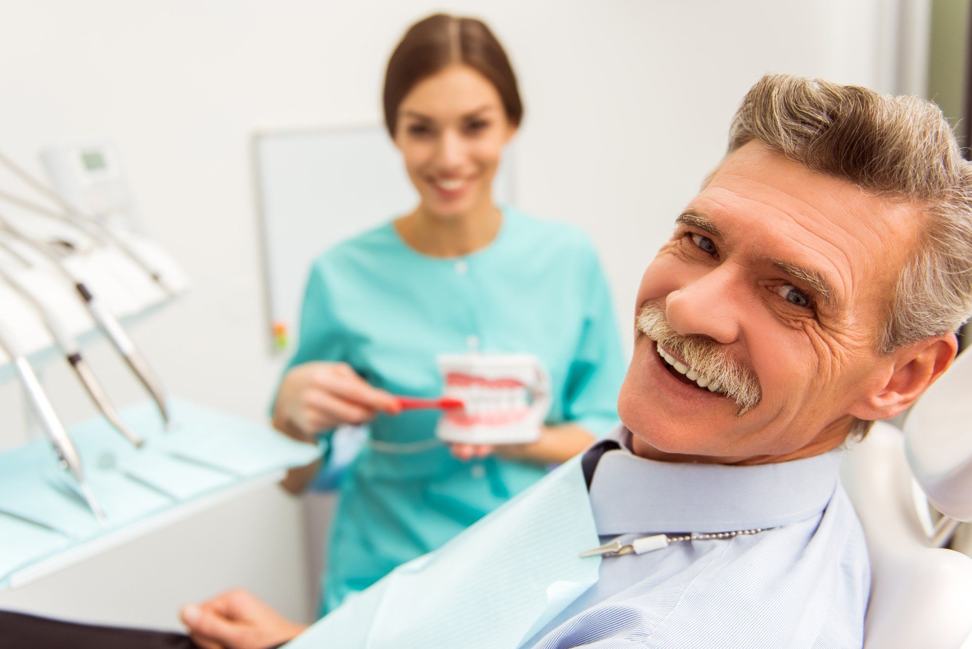 a man in a dental chair is smiling while a woman holds a model of teeth