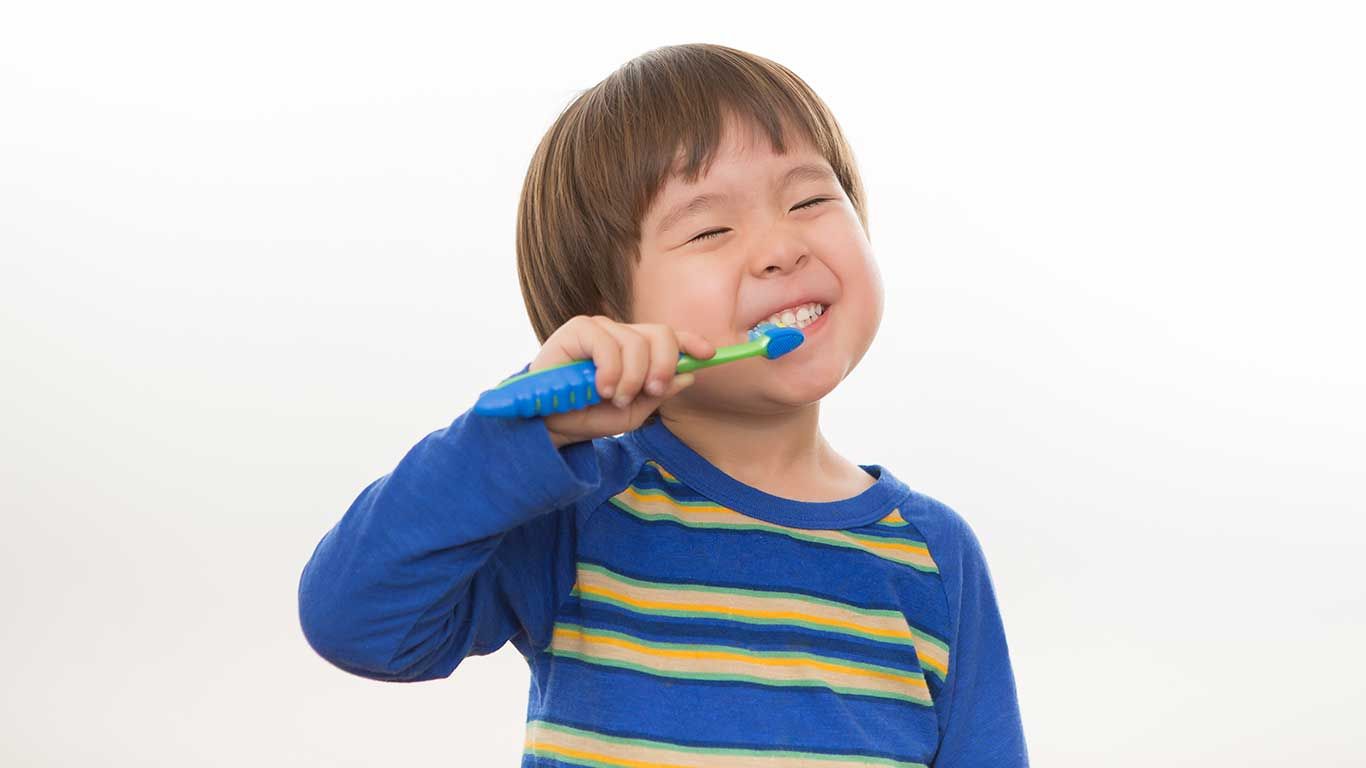 Young child brushes teeth, smiling, blue and yellow striped shirt.