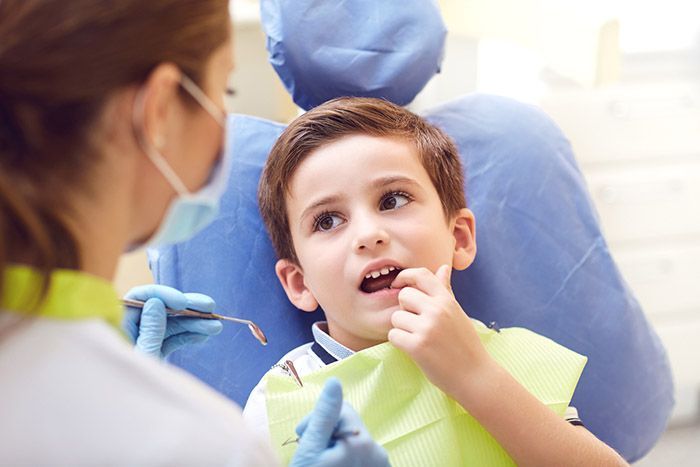 A young boy is sitting in a dental chair while a dentist examines his teeth.