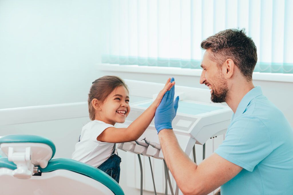 Dentist gives a high five to a smiling child in a dental office.