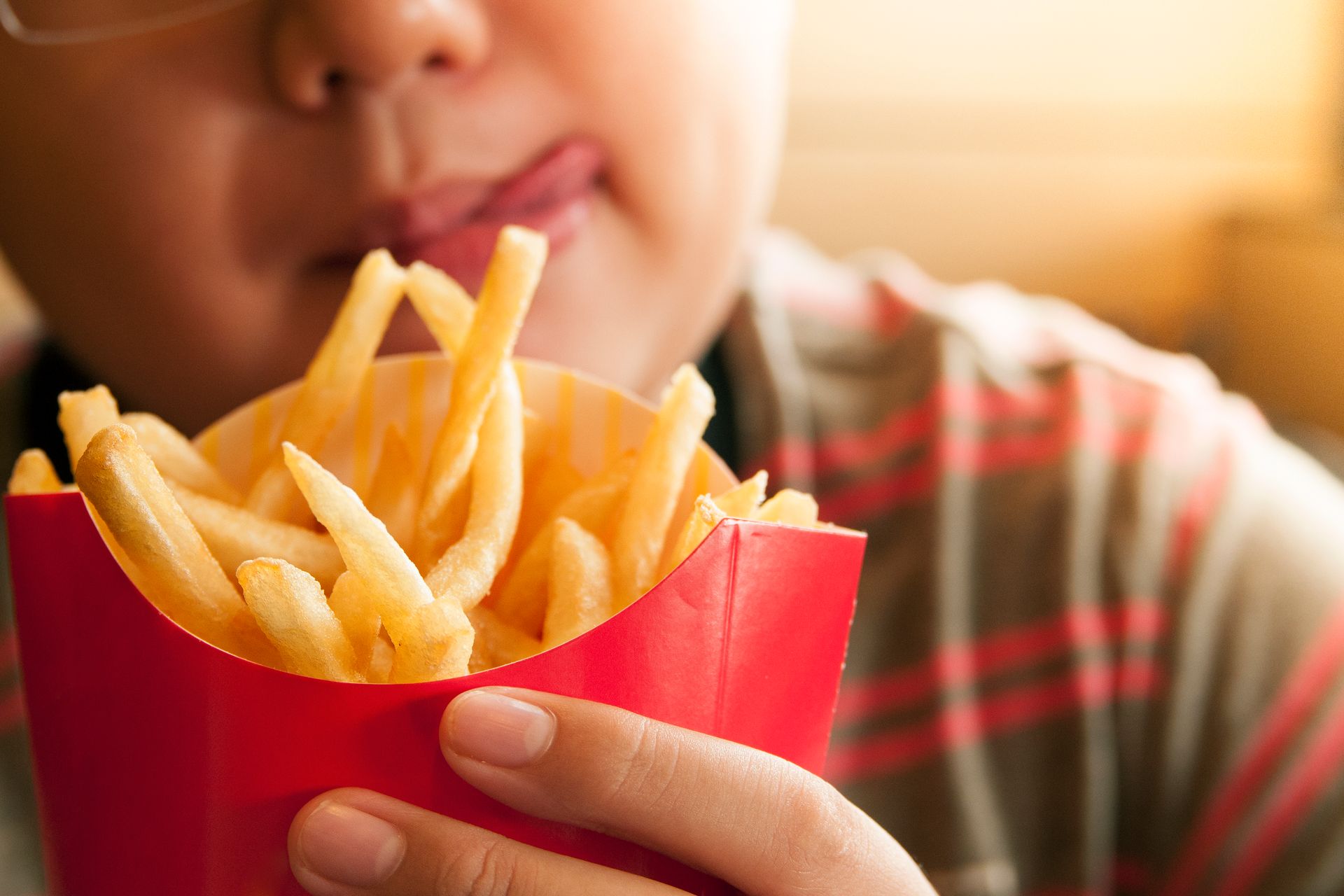 A person holds a red container of golden-brown french fries, licking their lips in anticipation.