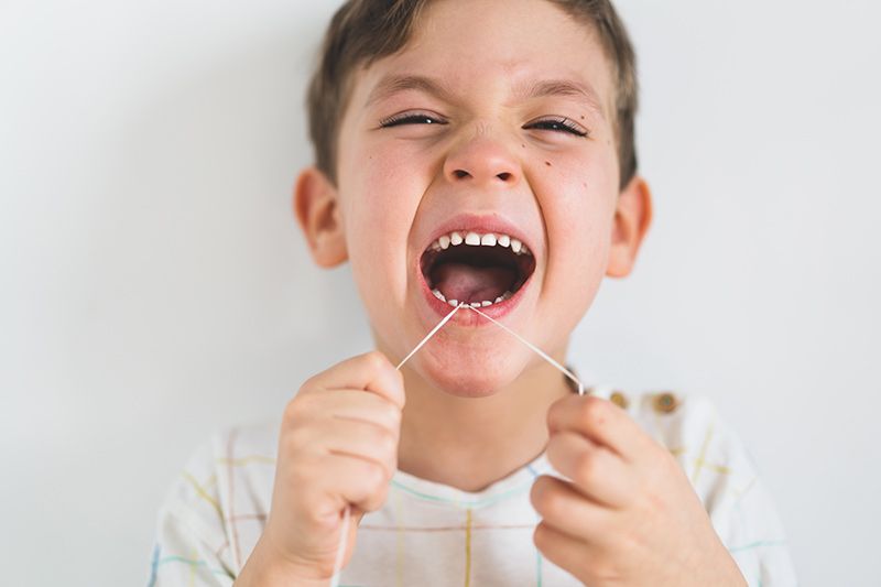 A young boy is flossing his teeth with a toothpick.