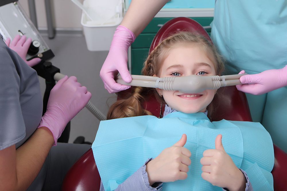 A little girl is giving a thumbs up while sitting in a dental chair.