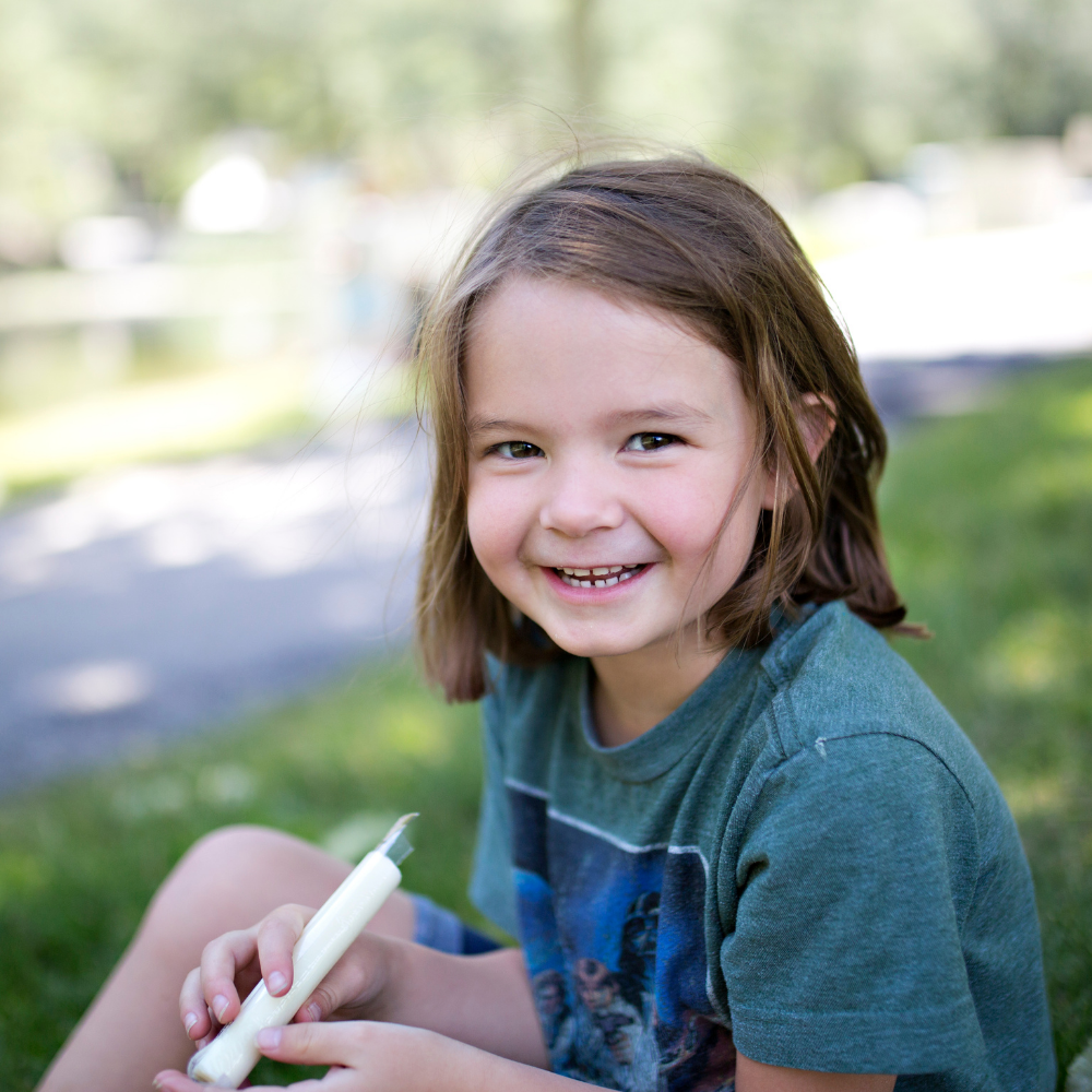 Kid sitting outside on grass and smiling. Kid playing with a toy outside.