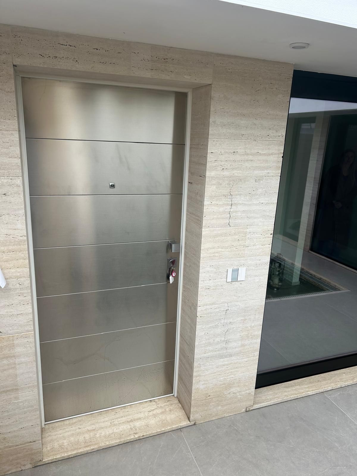 Porta in acciaio inossidabile incastonata in un muro di pietra chiara, accanto a una finestra in vetro.