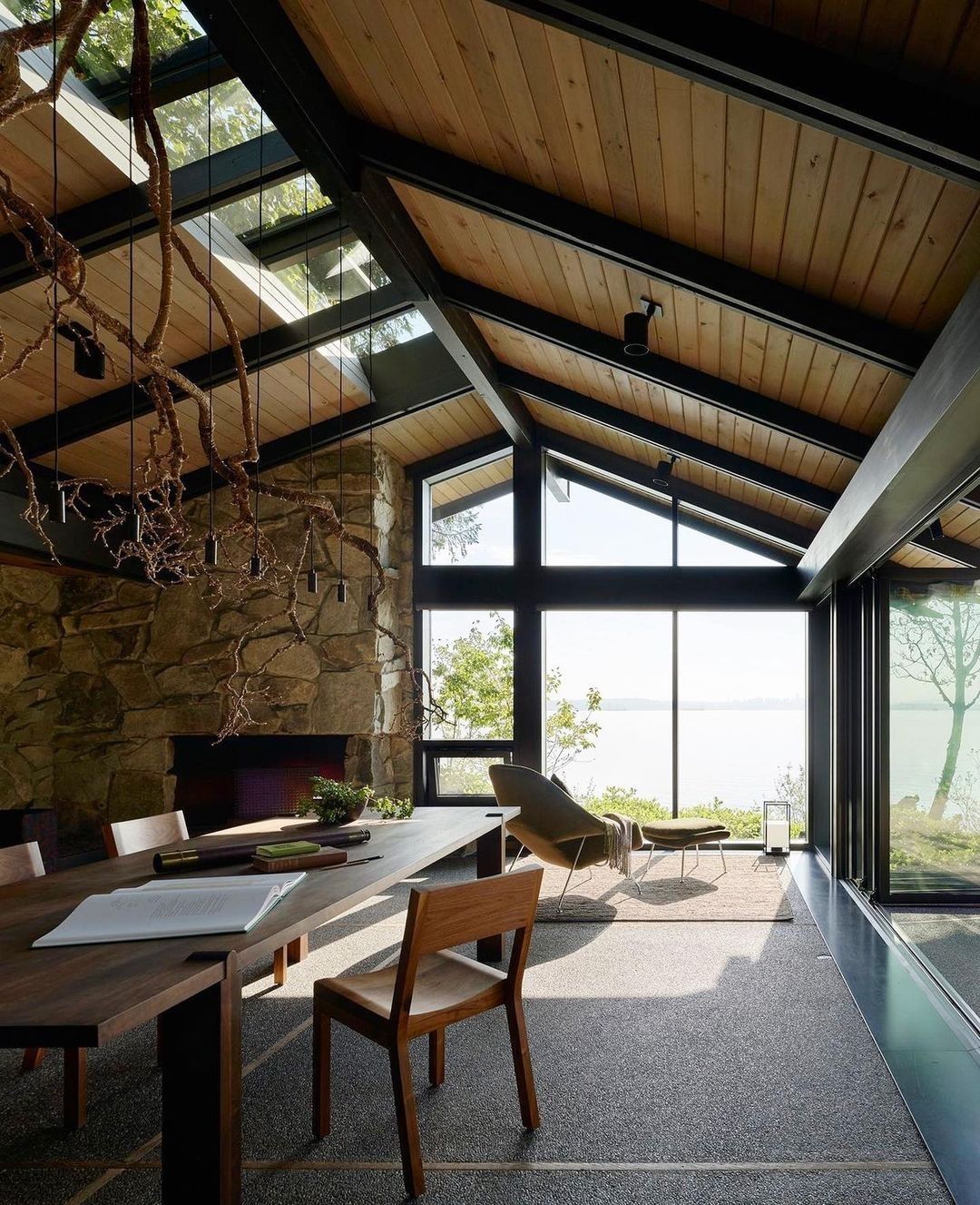 Zona pranzo con soffitto a volta in legno, camino in pietra e ampie finestre con vista sull'acqua.