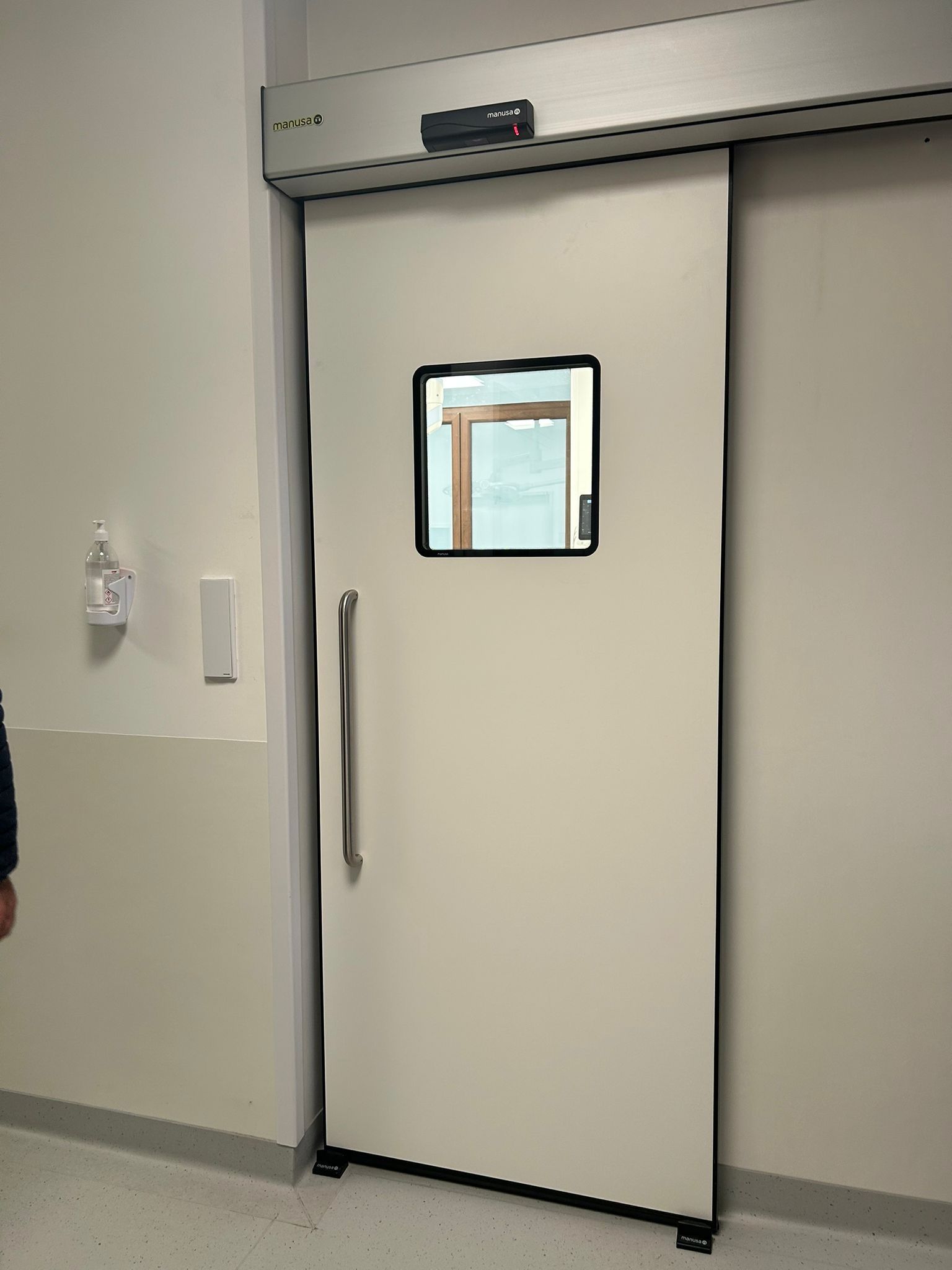 Corridoio con porte scorrevoli, pareti e pavimenti bianchi. Una porta è aperta, rivelando una stanza buia all'interno porte sicurezza ospedale Roma Mz Sistemi a Latina