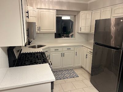 A kitchen with white cabinets , a stove , a refrigerator , and a sink.