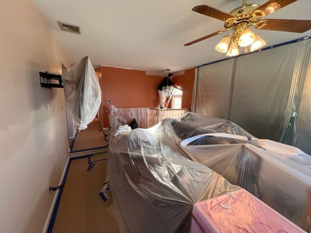 A room is being painted with plastic coverings and a ceiling fan.
