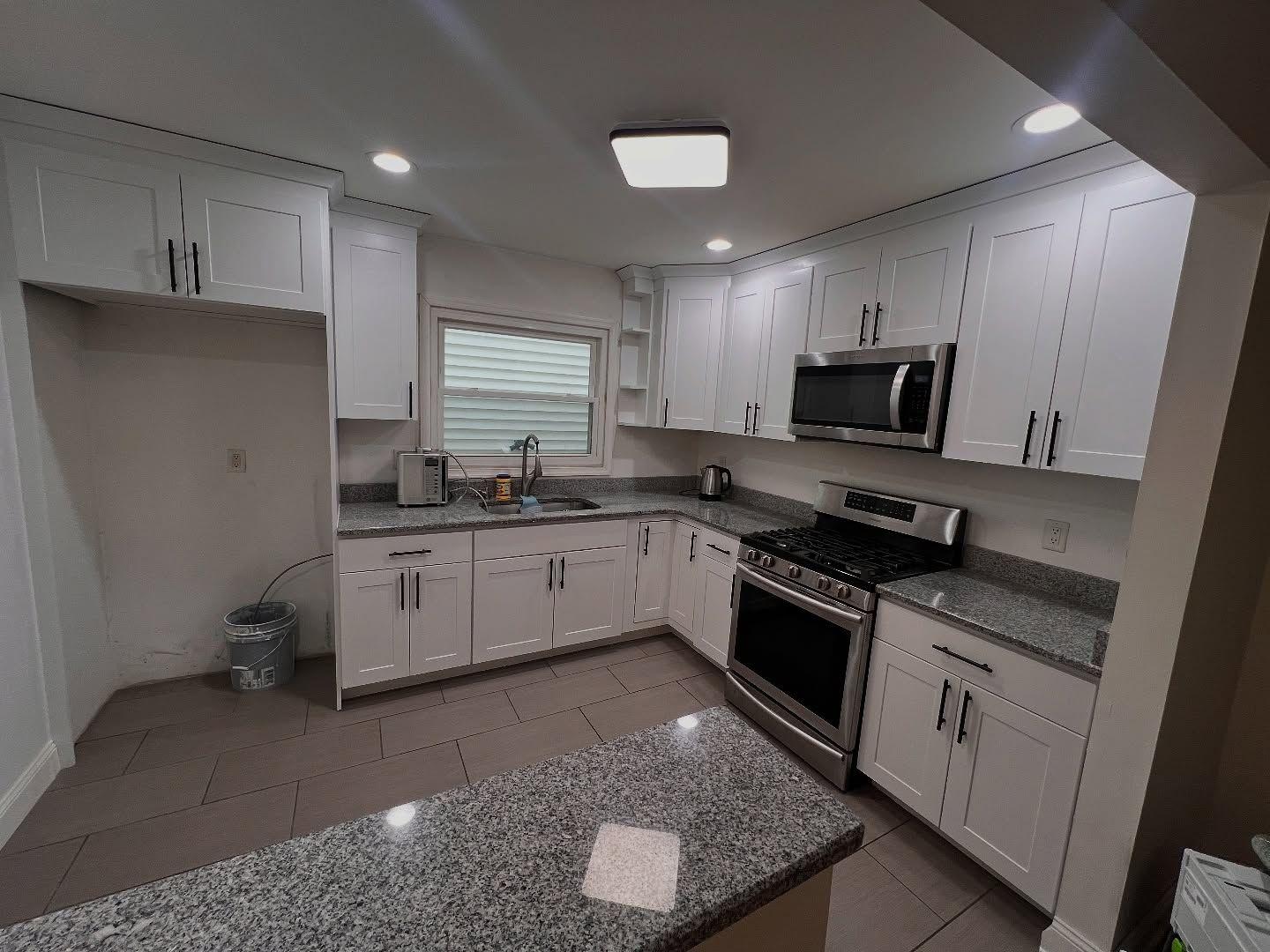 A kitchen with white cabinets , granite counter tops , stainless steel appliances and a window.