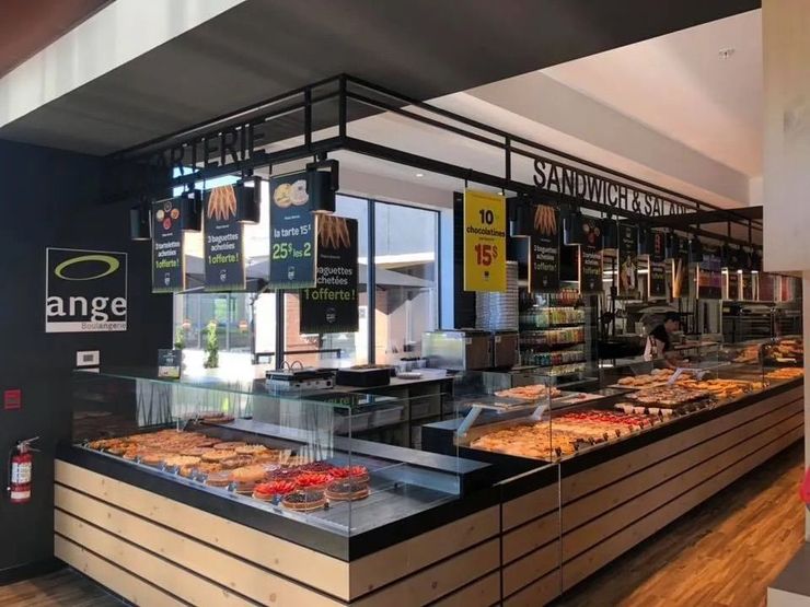 Un comptoir de boulangerie Ange avec des vitrines remplies de viennoiseries et de pains, et des menus affichés au-dessus des étagères.