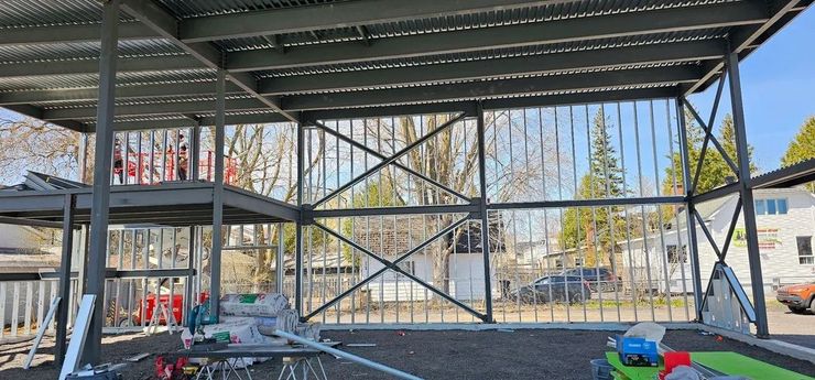 Une structure à ossature métallique en construction, montrant à l'extérieur des colonnes verticales, des poutres de plafond et des murs contreventés.