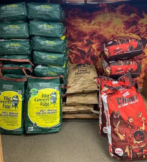 Bags of charcoal stacked on a store shelf. Brands include Big Green Egg, Royal Oak, and Jealous Devil.
