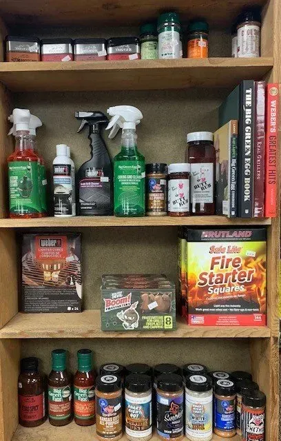 Wooden shelves holding various grilling supplies including sauces, spices, fire starters, and cleaning products.