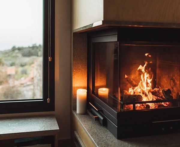 A fireplace with burning flames and two lit candles sits next to a window. The scene is warm and cozy.