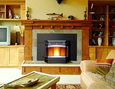 A pellet stove with a glowing fire sits in a wooden fireplace. The room has built-in shelves, a beige couch, and a coffee table.