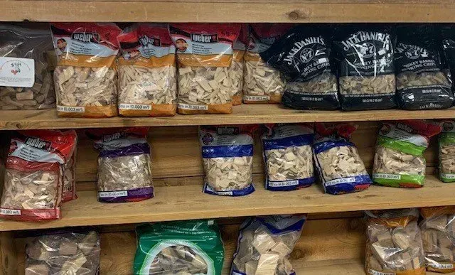 Wooden shelves displaying various bags of wood chips, including varieties with colorful labels.