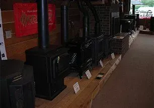 A row of black wood-burning stoves on display inside a store with wood paneling.