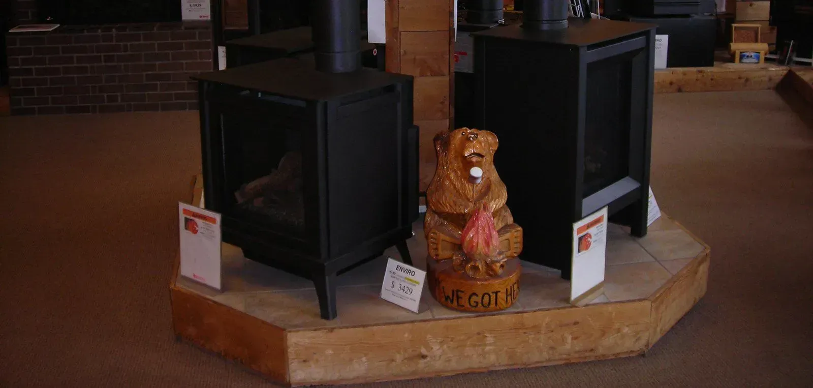 Two black stoves displayed on a wooden platform, with a carved bear statue holding a flame between them.