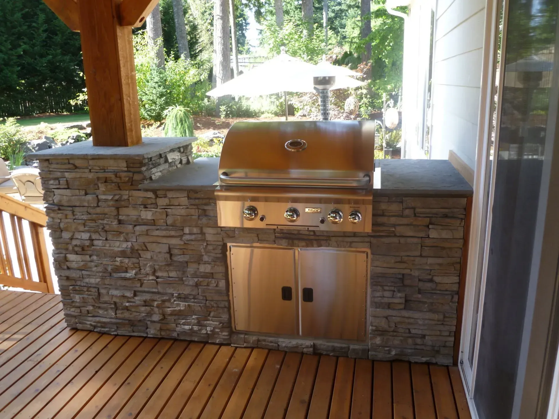 Outdoor kitchen with a built-in stainless steel grill and stone facade, set on a wooden deck.