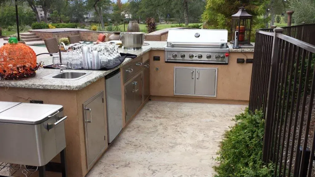Outdoor kitchen with a stainless steel grill, sink, and refrigerator. A large pumpkin decorates the counter.