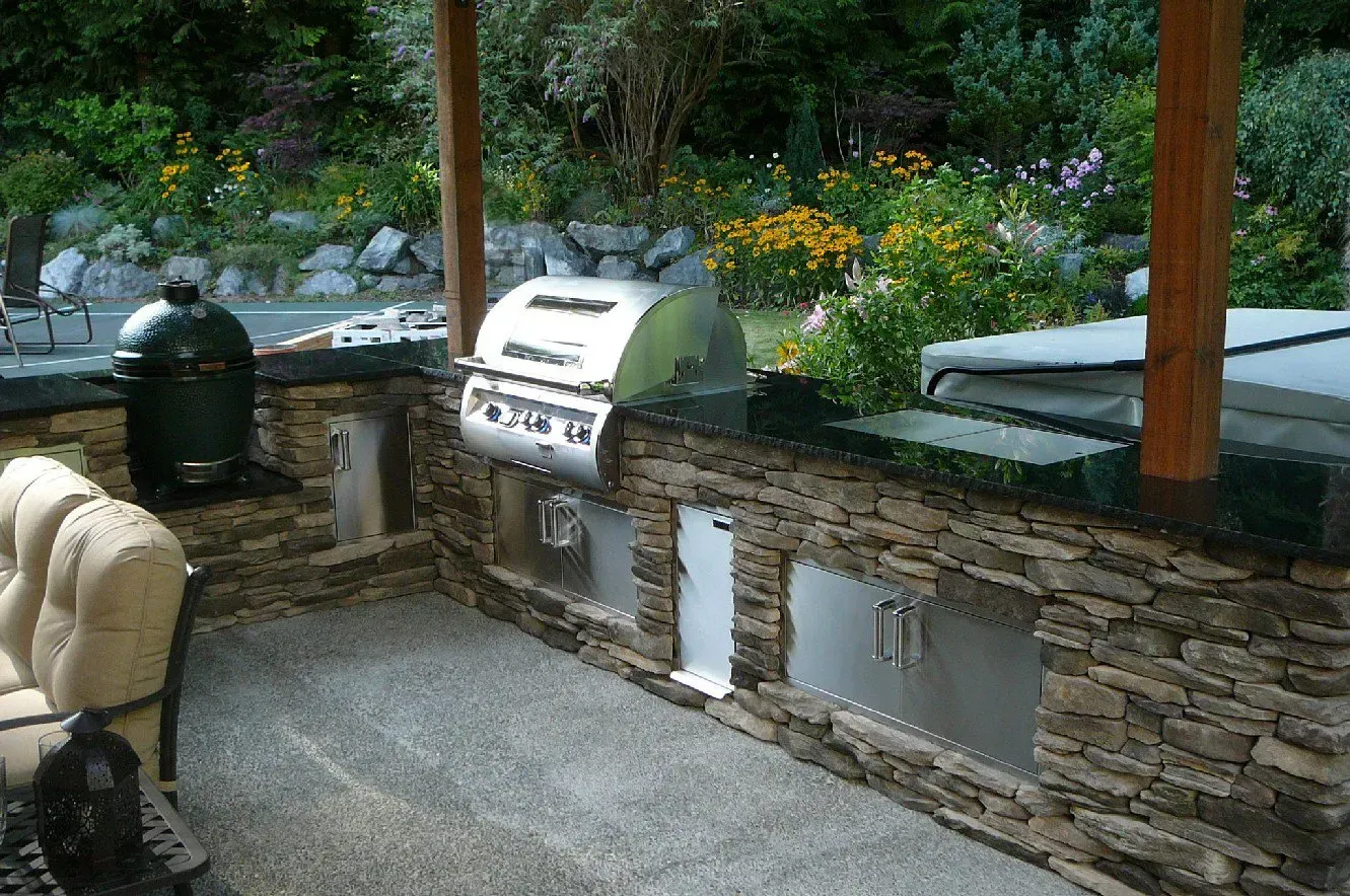 Outdoor kitchen with stone facade, featuring a grill, Big Green Egg, and stainless steel storage.
