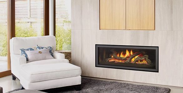 A modern living room with a fireplace. White chair by a window, fireplace against a light-colored wall with wooden cabinets.