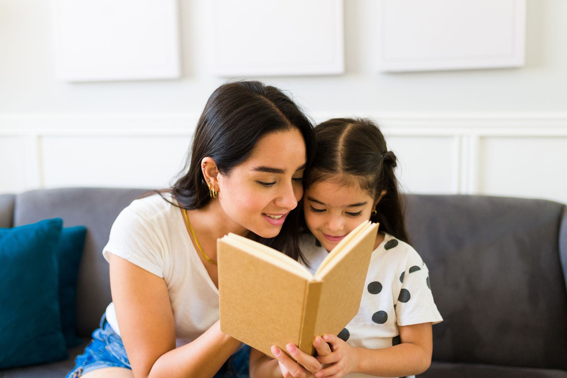 Woman and young girl reading a book together on a couch.