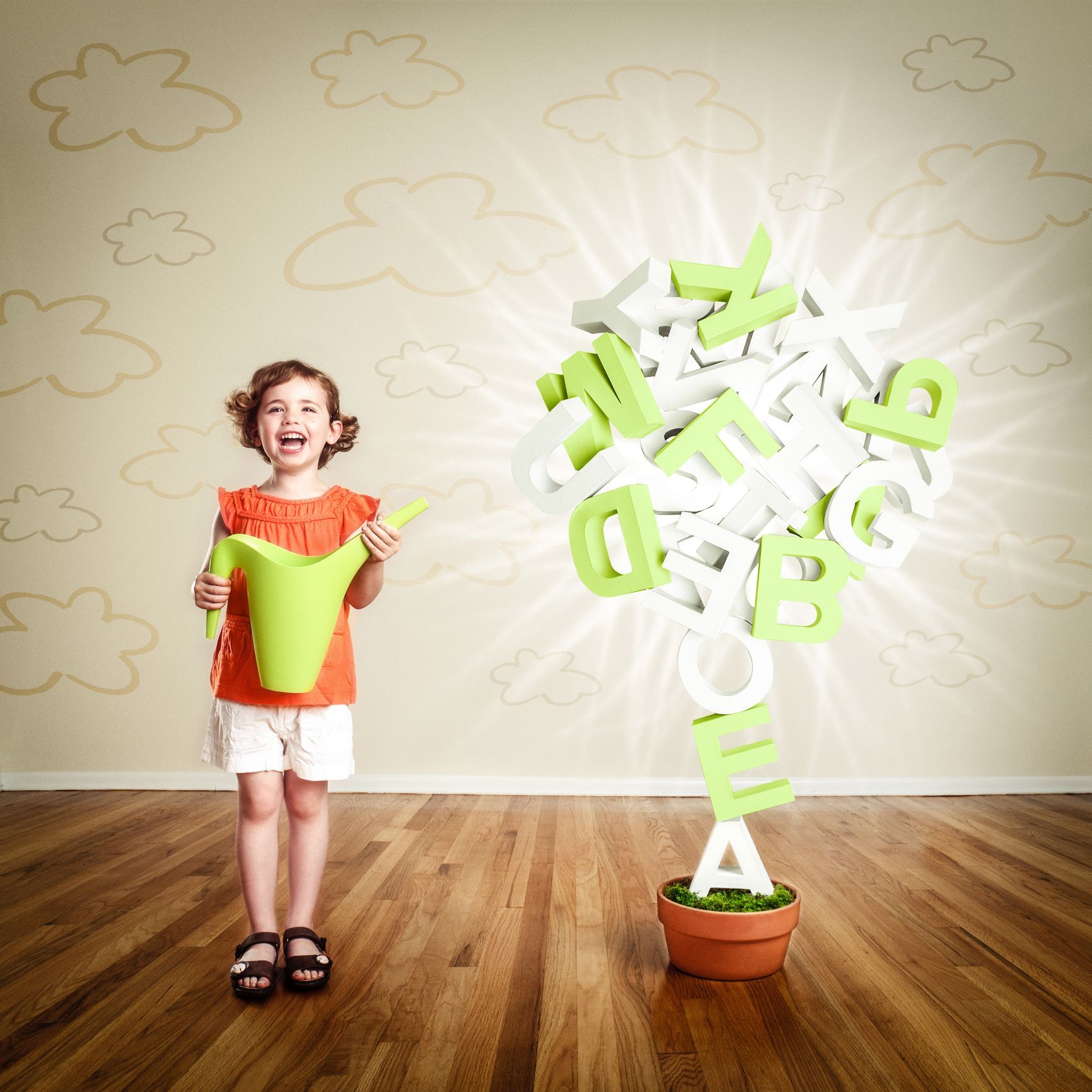 Young girl waters a tree made of letters. She stands in a room, with clouds on the wall. Young girl waters a tree made of letters. She stands in a room, with clouds on the wall.