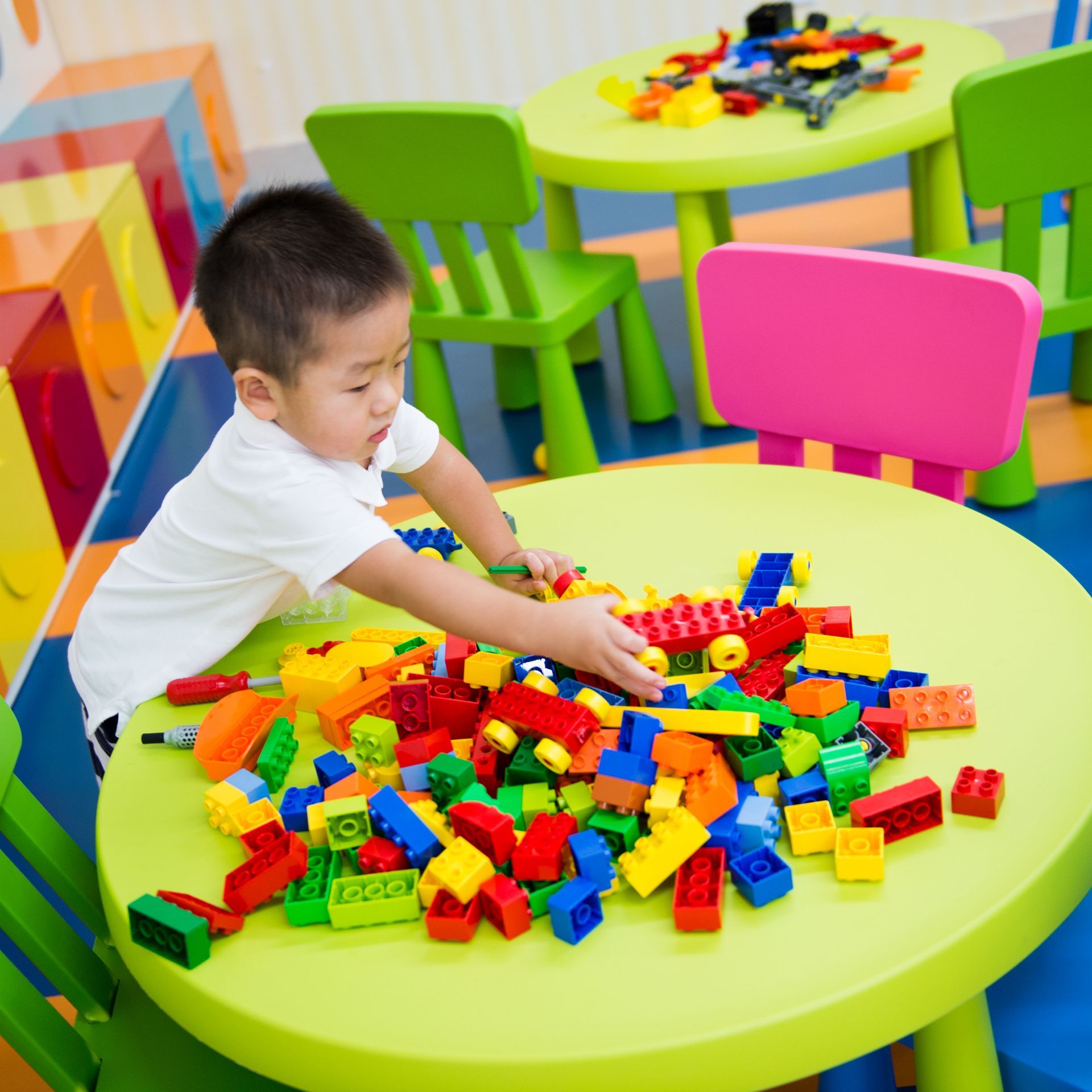 Boy playing with colorful building blocks on a green table in a playroom.