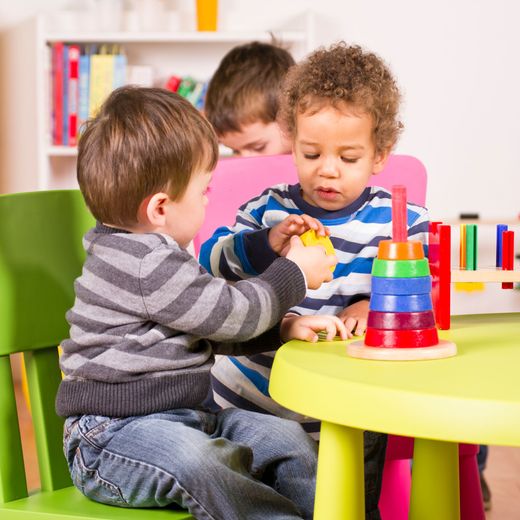 Three young children at a table playing with stacking rings and blocks in a colorful playroom.