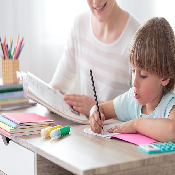 A woman and a young child study at a desk. Child is writing, woman is reading.