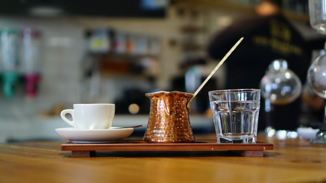 a cup of coffee and a glass of water on a wooden tray on a table .