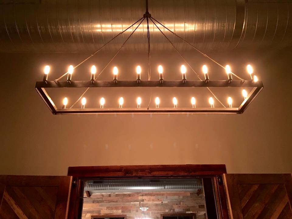 Rectangular chandelier with multiple exposed bulbs, hanging above a wooden door frame and paneled wall.