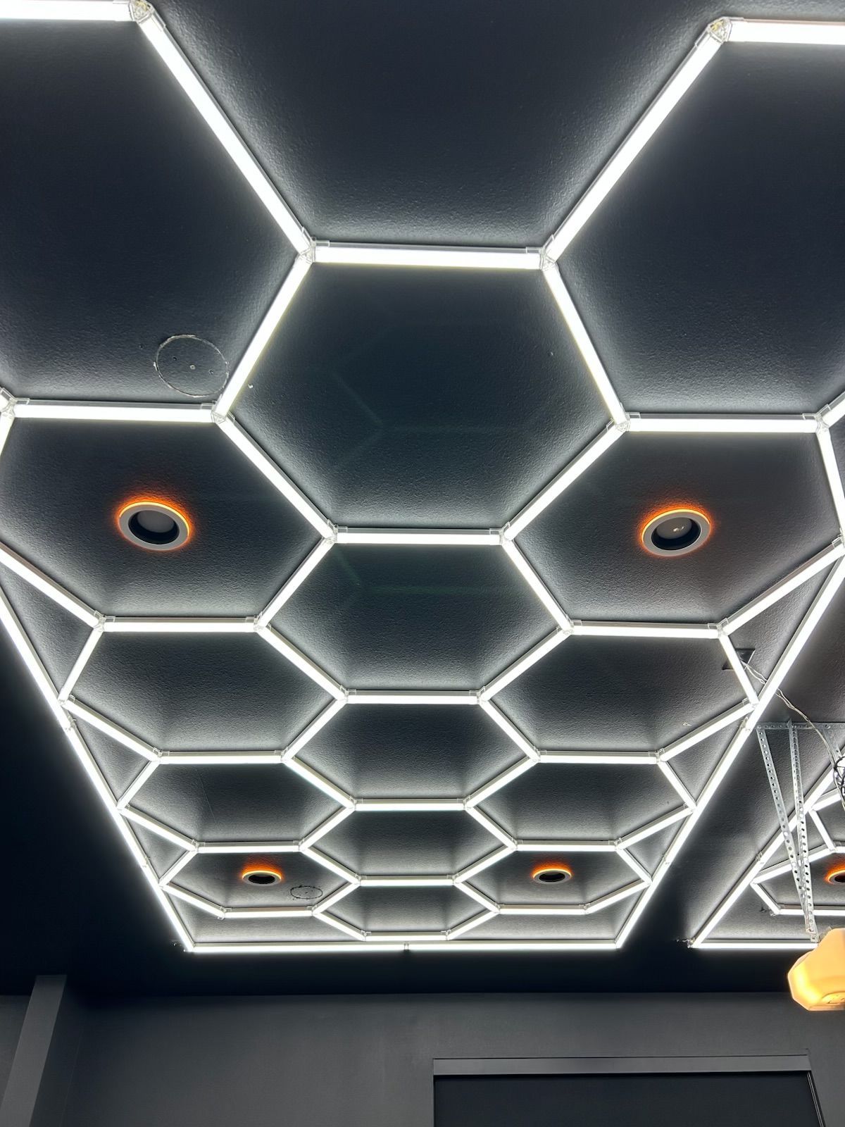 A dark ceiling features a geometric honeycomb grid of white LED lights with several recessed, orange-lit spotlights.