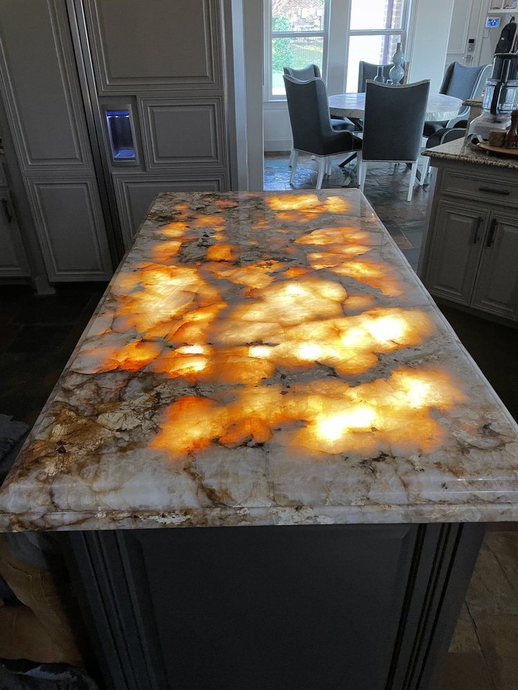A backlit, glowing orange and white onyx kitchen island countertop with a marble-like pattern in a modern kitchen.