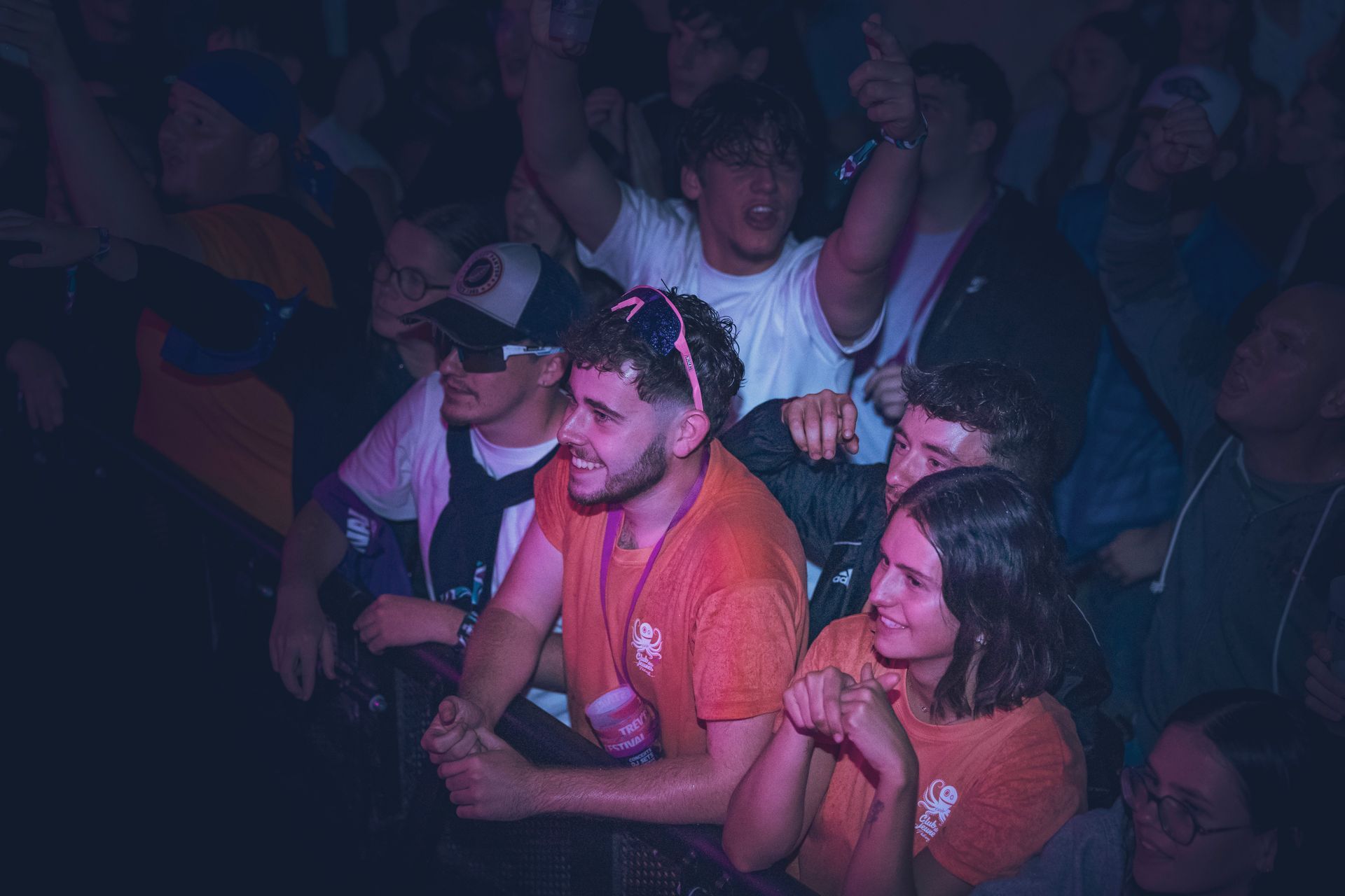 Une foule de personnes dans une lumière tamisée aux tons bleutés lors d'un événement, avec plusieurs individus souriants au premier plan.