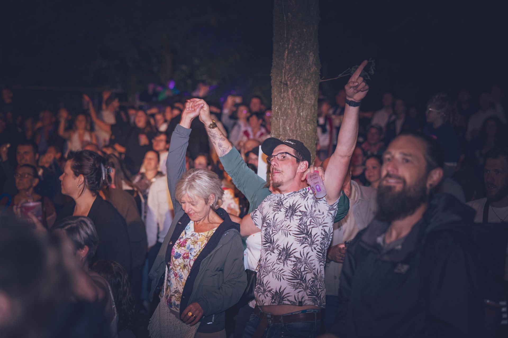 Une foule apprécie un concert nocturne en plein air, deux personnes au premier plan dansant les bras levés.