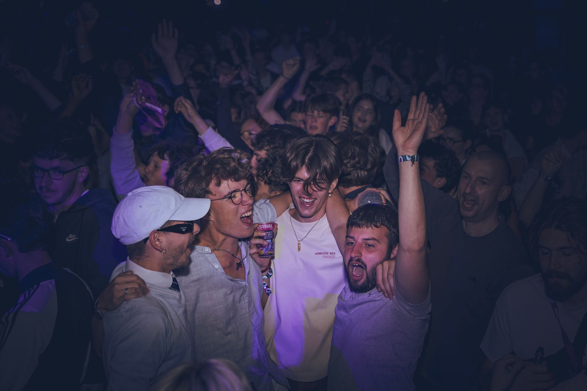 Une foule acclame un groupe lors d'un concert en salle faiblement éclairé, avec un groupe au premier plan chantant dans un microphone.