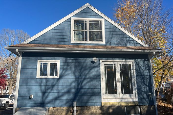 Blue house with white trim and a steep roof in a sunny residential neighborhood