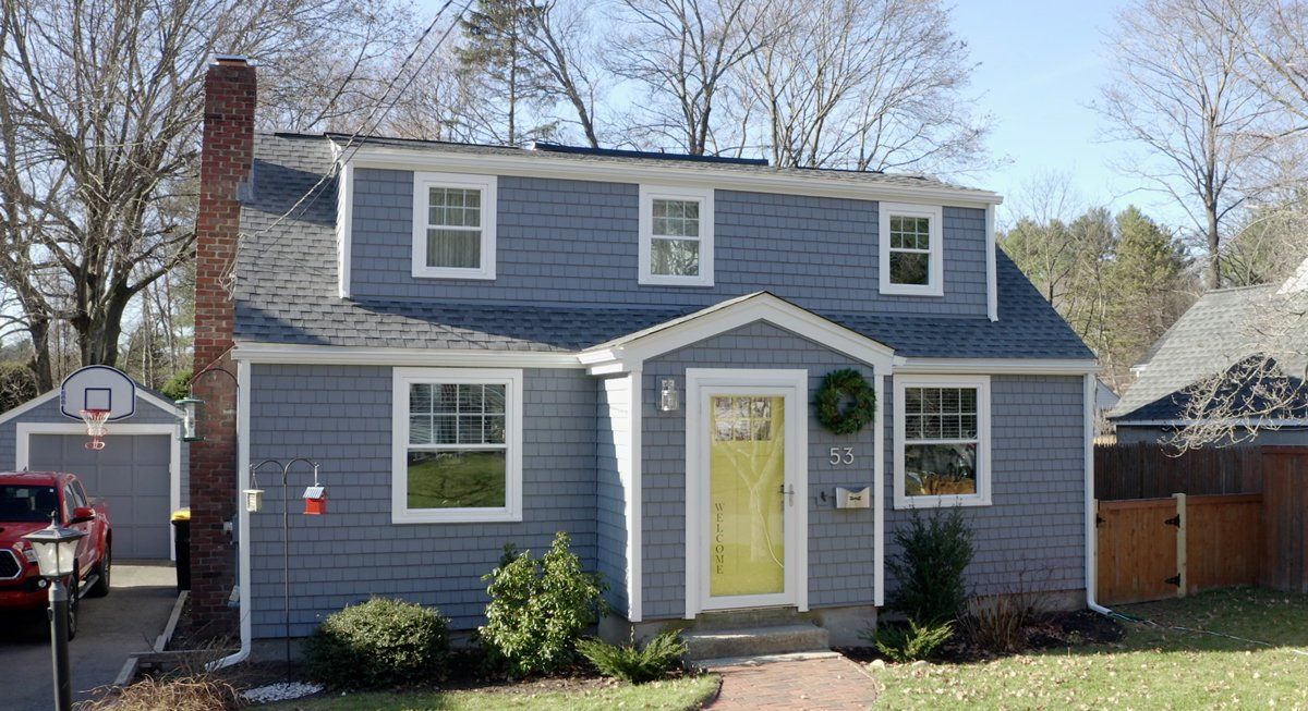 Bruin Remodeling Group |A gray house with a yellow door and a basketball hoop in the backyard.