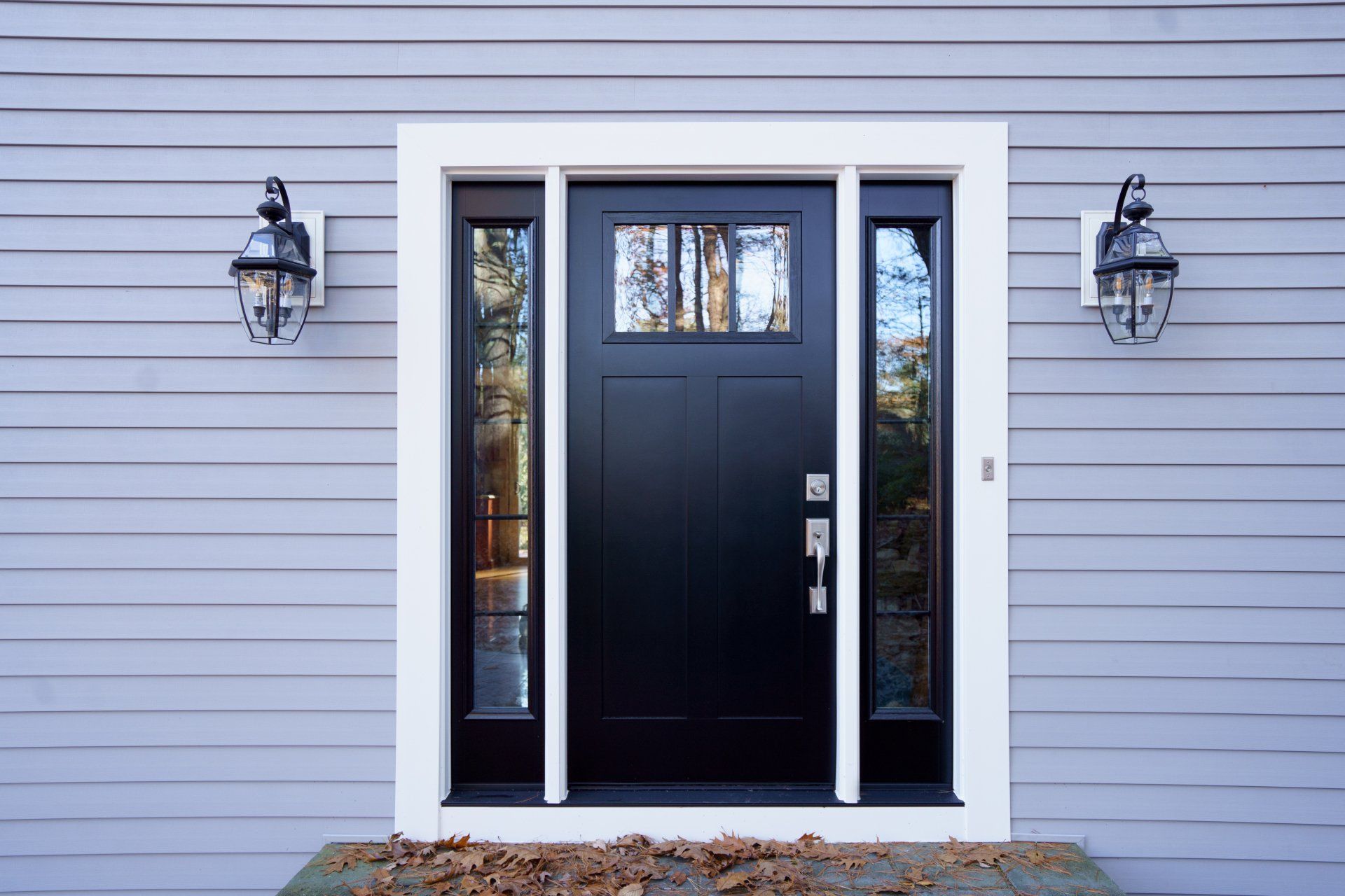 A black front door with a white trim is on a gray house.