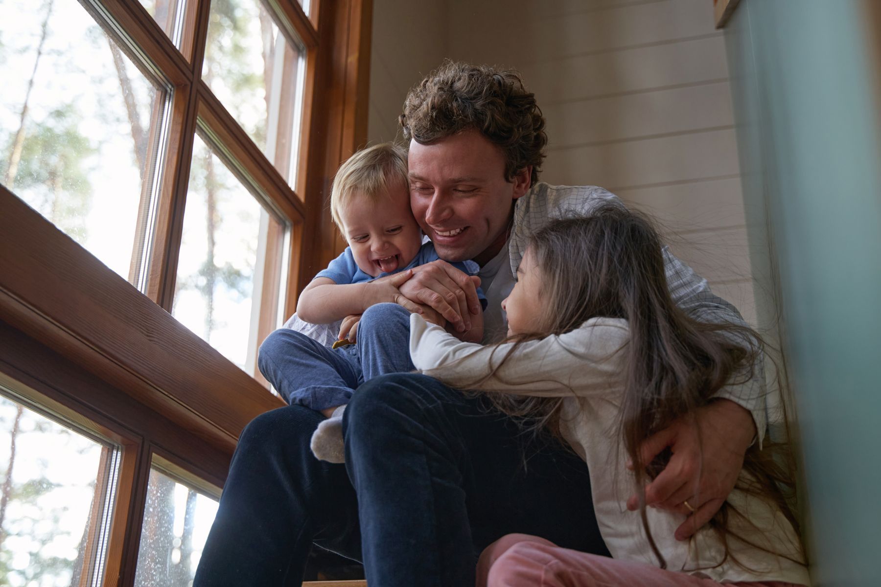 A man is sitting on a window sill with two children.
