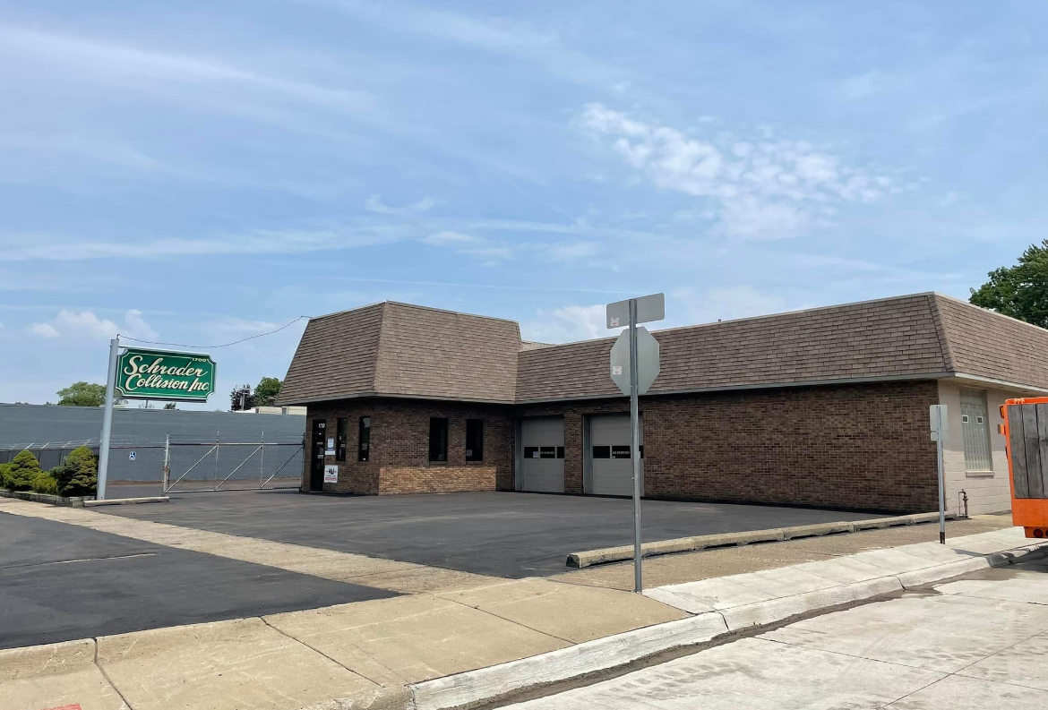 Brick restaurant building with green sign on a street corner under a bright blue sky