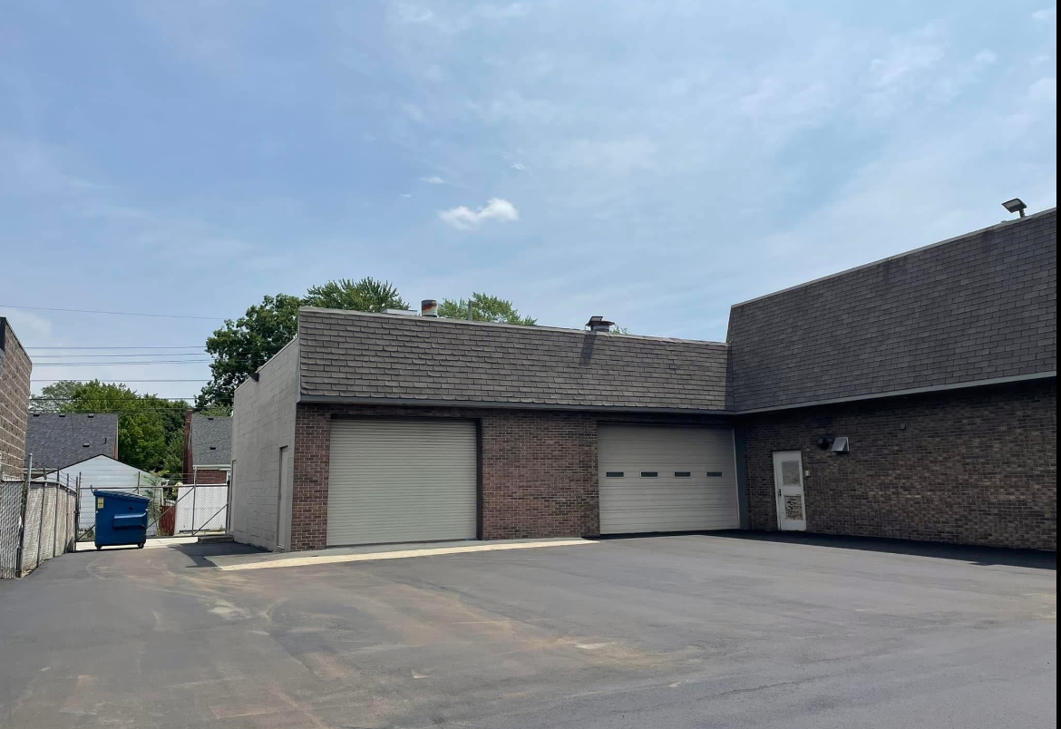 Empty parking lot in front of a low brick building with gray garage doors under a cloudy sky