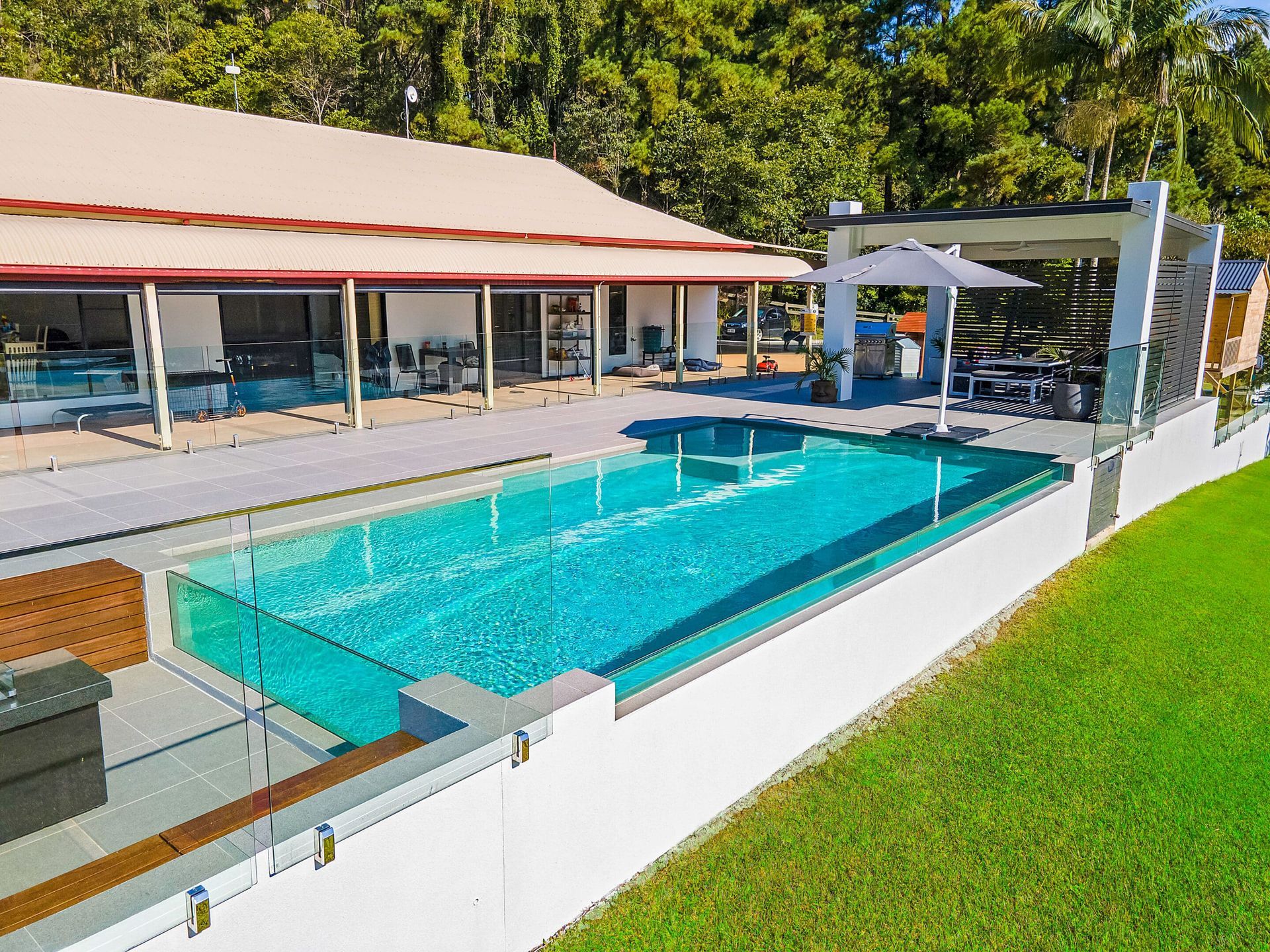 A Large Swimming Pool is Surrounded by a White Fence in Front of a House — Pools By Design in Warana, QLD
