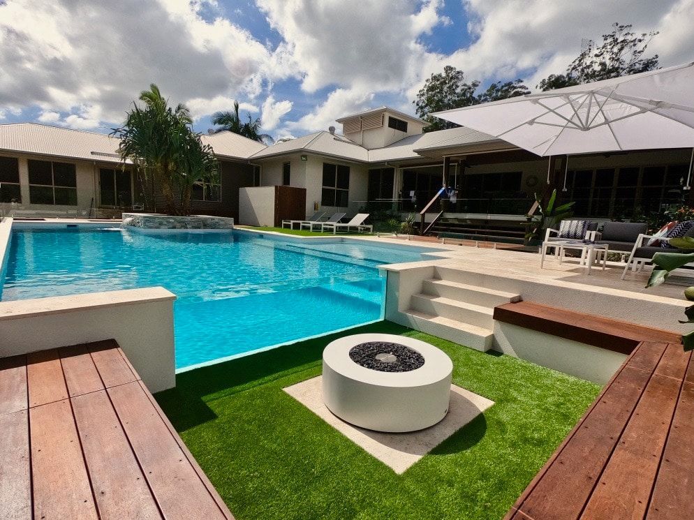 A Large Swimming Pool With a Fire Pit in the Middle of It — Pools By Design in Warana, QLD