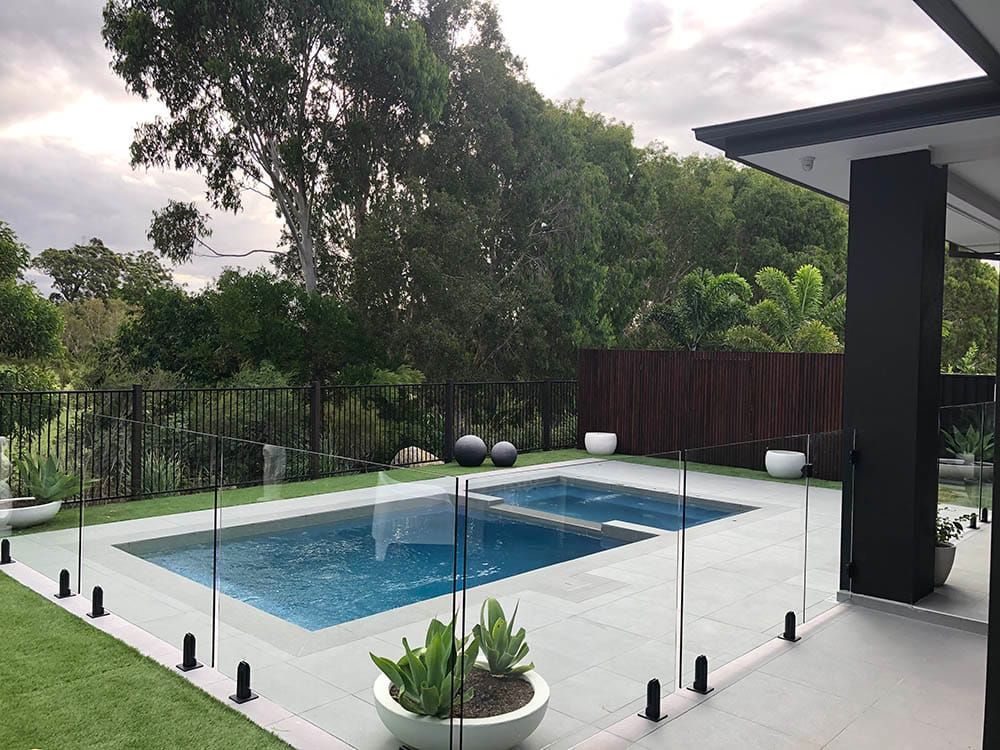 A Large Swimming Pool is Surrounded by a Glass Fence — Pools By Design in Warana, QLD